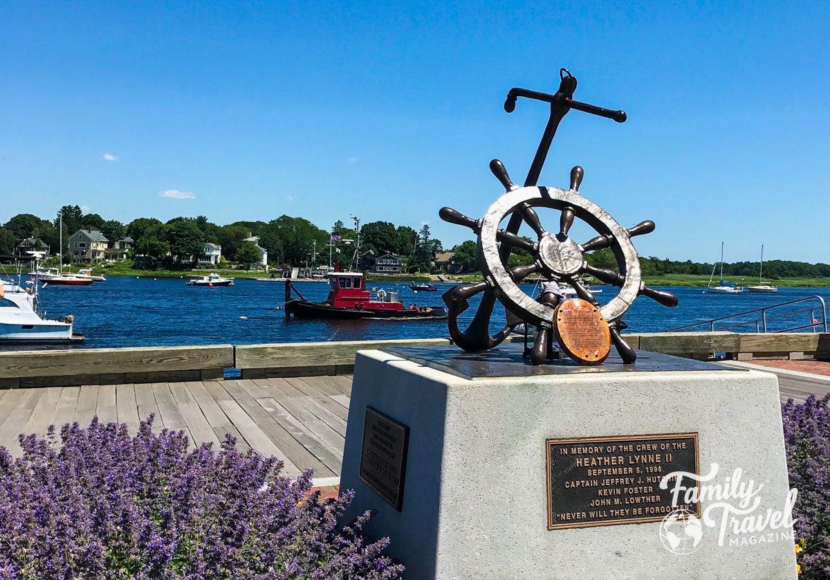 Anchor statue on waterfront with boats and flowers