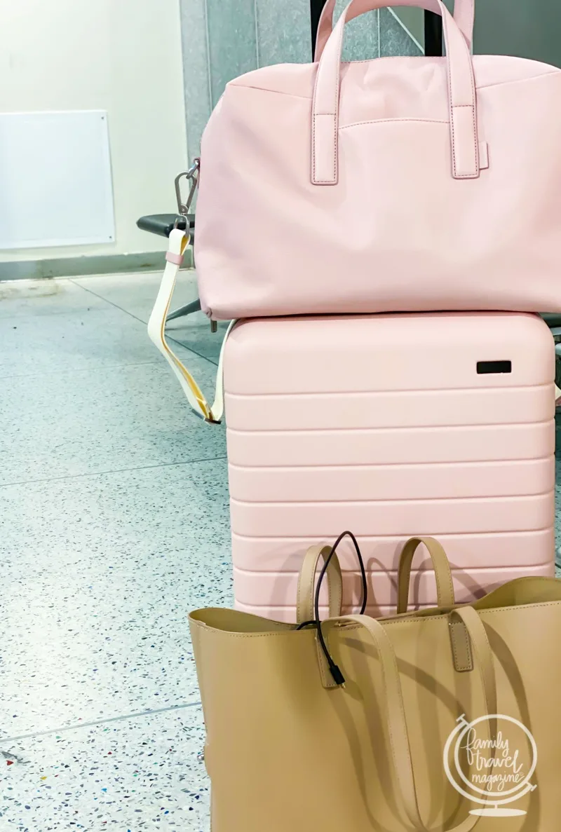 Pink duffle on top of roller suitcase with tote in the foreground