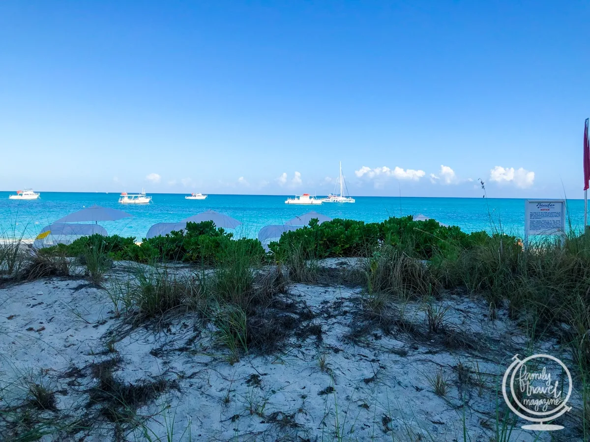 The beach at Beaches Turks and Caicos resort with boats in the water and dunes in the foreground