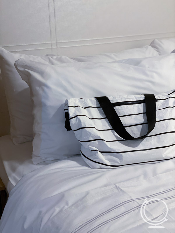 Beach bag on bed with white linens