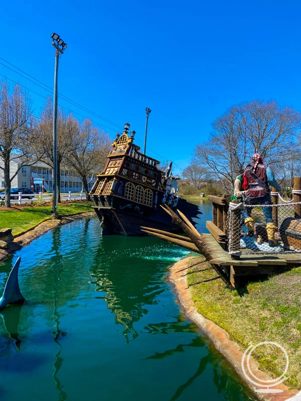 Mini sunken pirate ship in a pond with pirate statues nearby