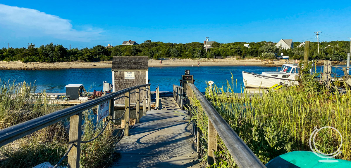 Boat docked at the side of a pier with a small wooden building - view from Sesuit Harbor Cafe, one of the best restaurants on Cape Cod