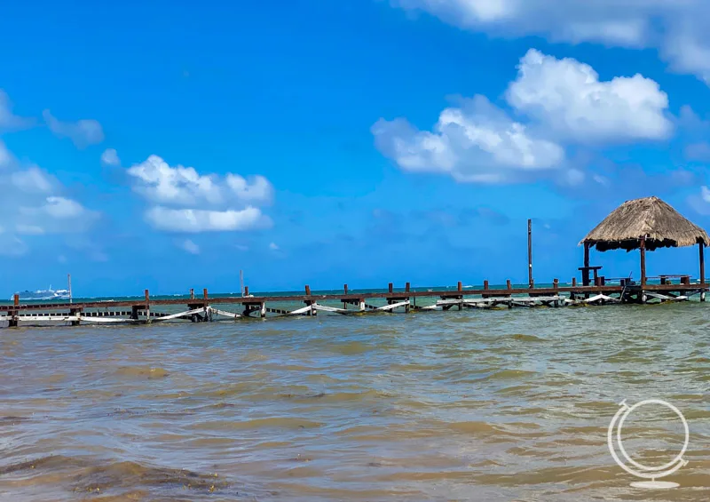 Pier over sea with a hut at the end. Cruise ship can be seen in the distance. 