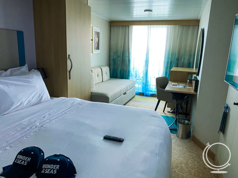 A balcony stateroom with king bed, pull out couch, and hats on the bed. 
