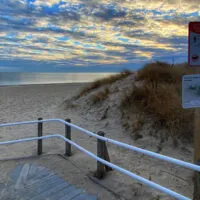 Beach at sunset with two warning signs, a blue/orange sky and a sandy boardwalk