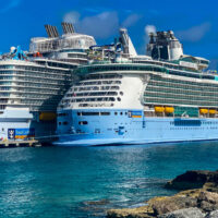 Royal Caribbean's Wonder of the Seas and Freedom of the Seas docked with rocky coast in the foreground. oreground.
