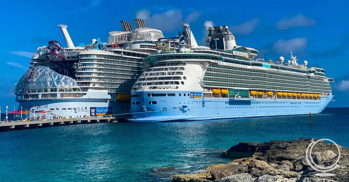 Royal Caribbean's Wonder of the Seas and Freedom of the Seas docked with rocky coast in the foreground. oreground.