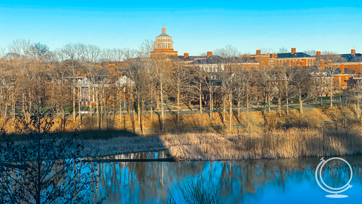The University of Rochester's River Campus from a distance with the Genesee River and bare trees in the foreground. 