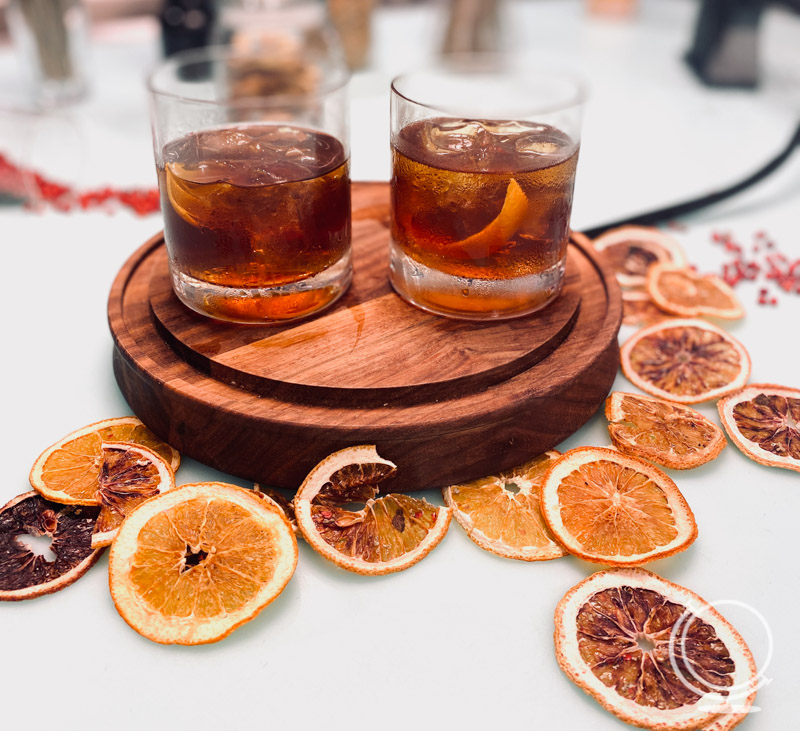 Two drinks on a smoker with dried orange peels surrounding it. 