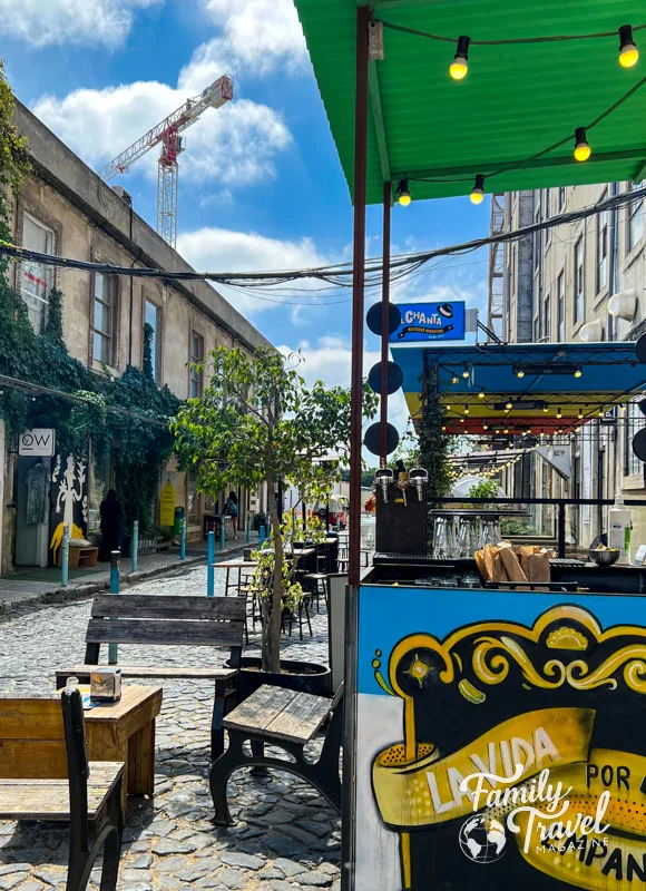 Building with vines on cobblestone pedestrian street with colorful restaurant in the foreground