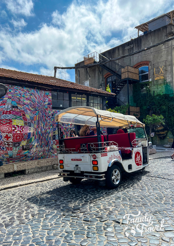 Red and white tuk tuk on cobblestone street next to colorful building