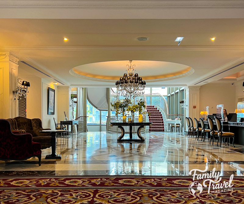 Lobby with big chandelier, staircase in back, glass table, check-in desks
