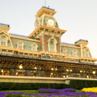 The Magic Kingdom railway station at park entrance with purple and yellow flowers in front of it.