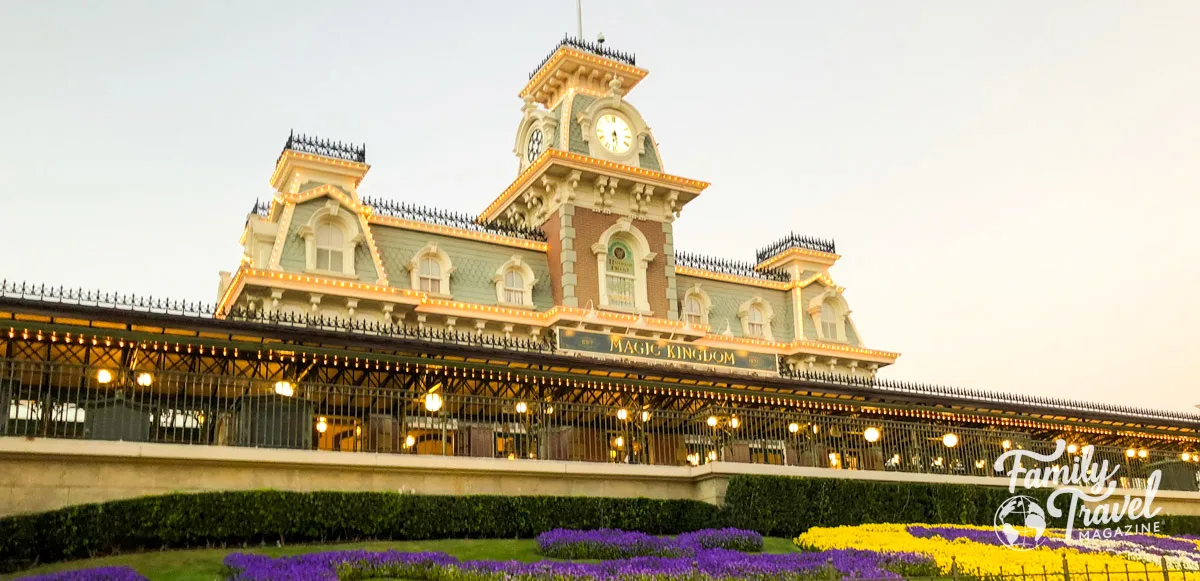 The Magic Kingdom railway station at park entrance with purple and yellow flowers in front of it. 