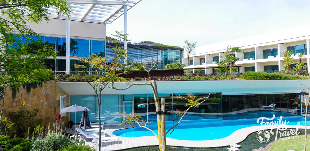 Lower level outdoor pool with upper level gardens, in front of a building with hotel room balconies