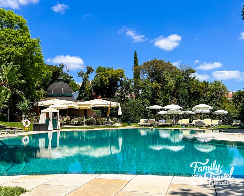 Outdoor pool with chairs, umbrellas, outdoor cafe surrounded by trees