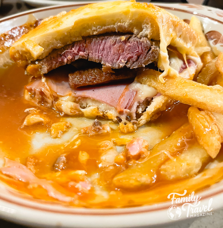 Francesinha sandwich cut in half with fries, cheese, steak, ham, and sausage