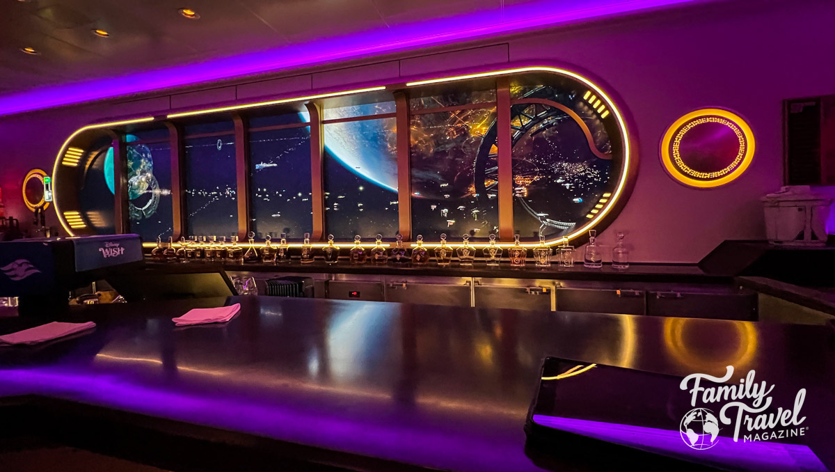 The bar at Star Wars Hyperspace Lounge with bottles along the counter and screen/window into space. 