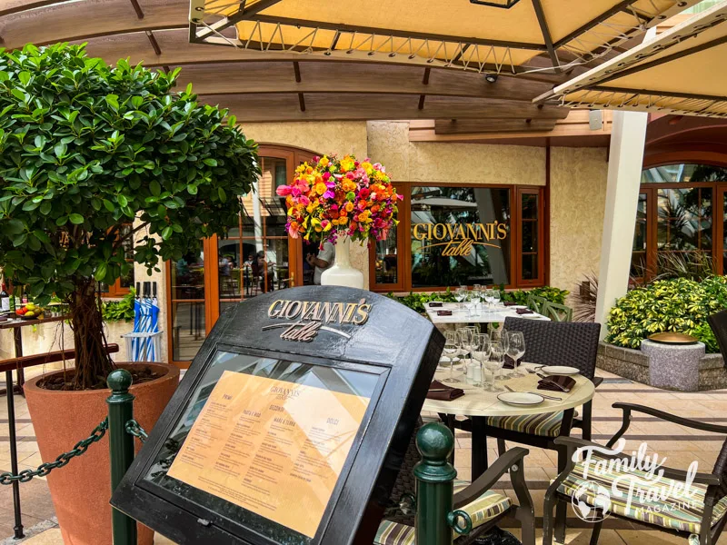 Exterior of Giovanni's Table, with menu, tables, and chairs, and flowers