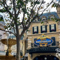 The outside of Remy's Ratatouille Adventure with a tree and fountain in the foreground