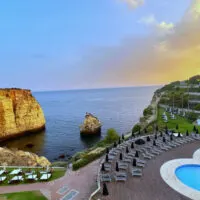Pool with lounge chairs overlooking waterfront cliff and caves at sunset
