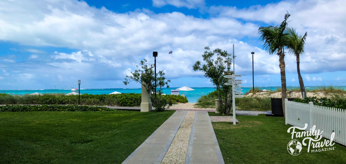 Path leading to beach with turquoise waters, beach chairs, and umbrellas