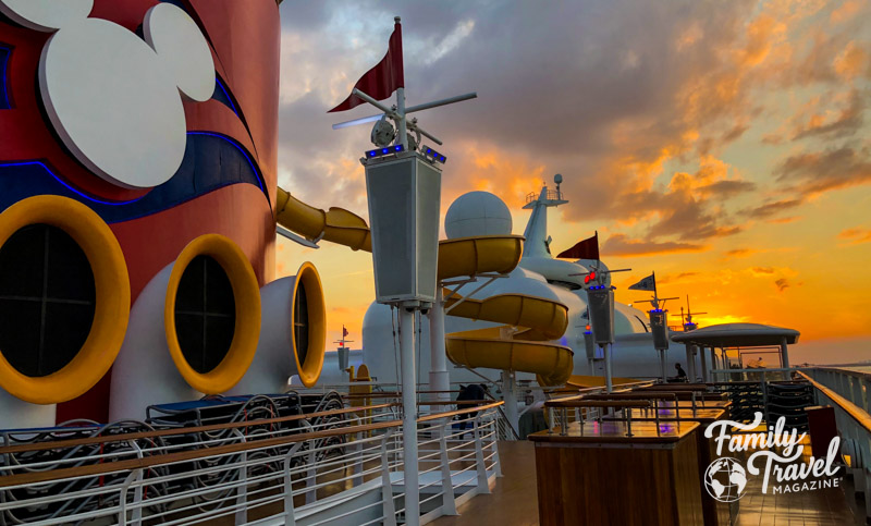 Golden sunset above the deck of the Disney Magic with the funnel and a waterslide in the foreground