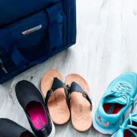 three pairs of shoes (loafers, sandals, sneakers) in front of carry on bag
