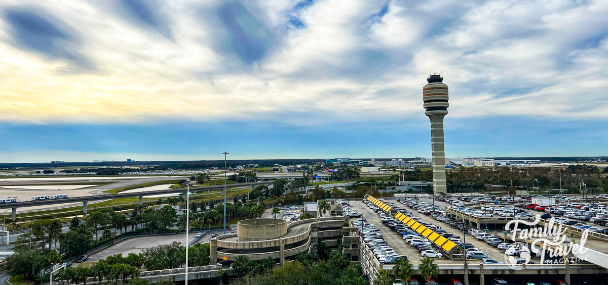 Exterior view of airport with tower, runway, and parking garage. 