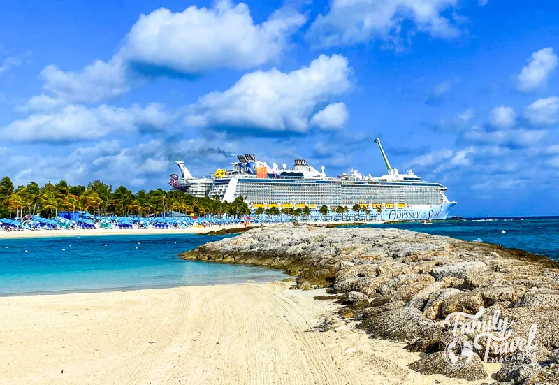 Odyssey of the Seas docked at beach with water, umbrellas, beach chairs, and rocks