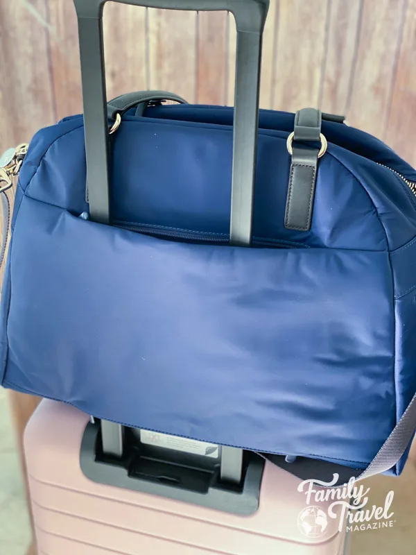 Blue carry on duffel on handle of pink roller suitcase