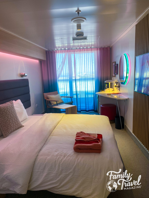 Cruise ship stateroom with small table, chair, bed, mirror