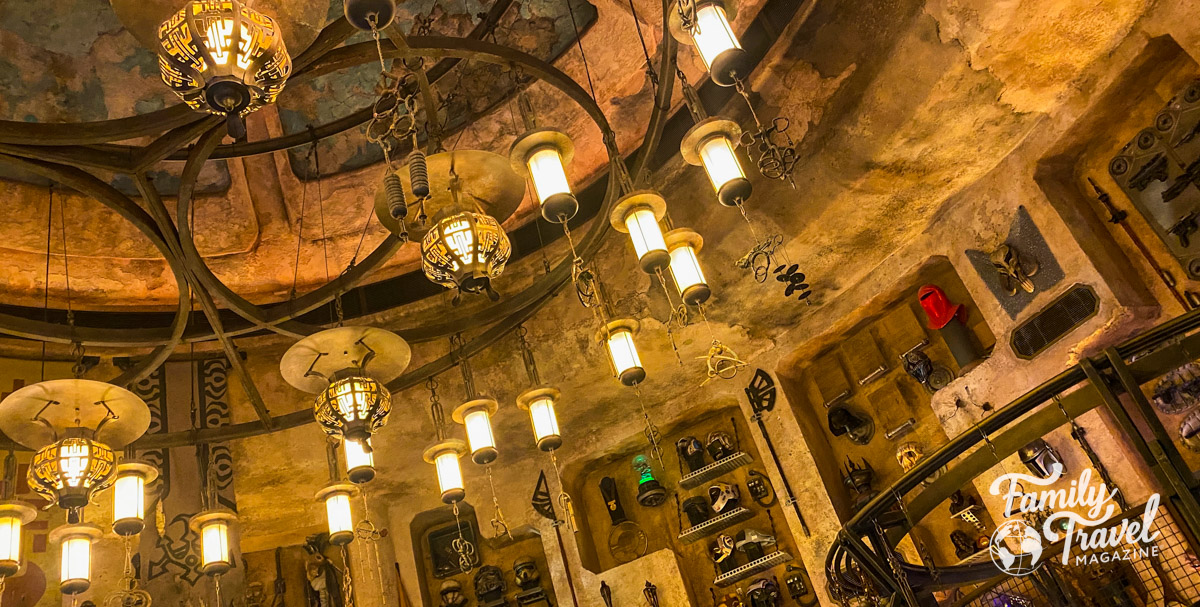 Star Wars: Galaxy's Edge building interior with Star Wars gadgets, masks, swords, and other items on wall with Star Wars themed lamps on ceiling