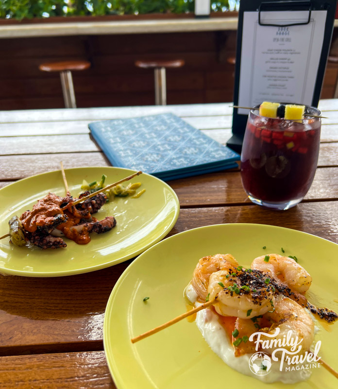 Octopus and shrimp dishes and a sangria on a table in front of a blue menu 