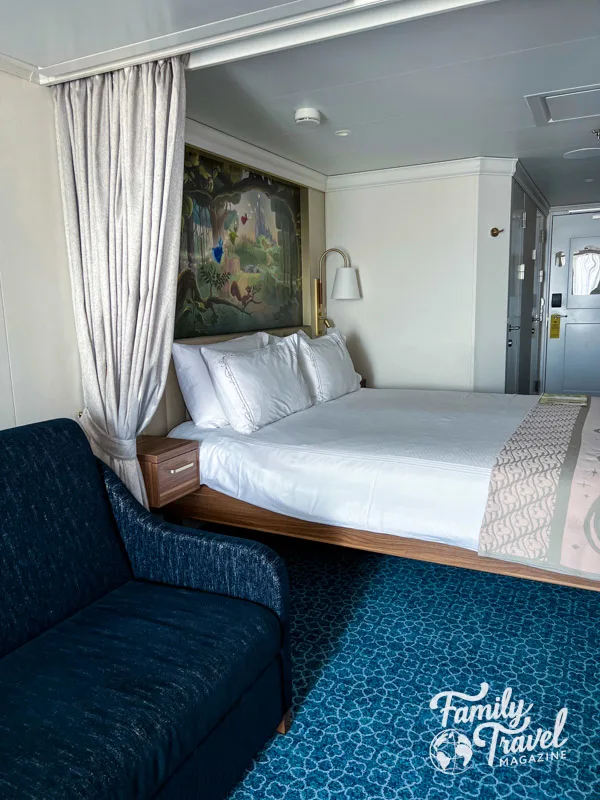 Convertible sofa and queen bed with privacy curtain in a Disney Wish stateroom