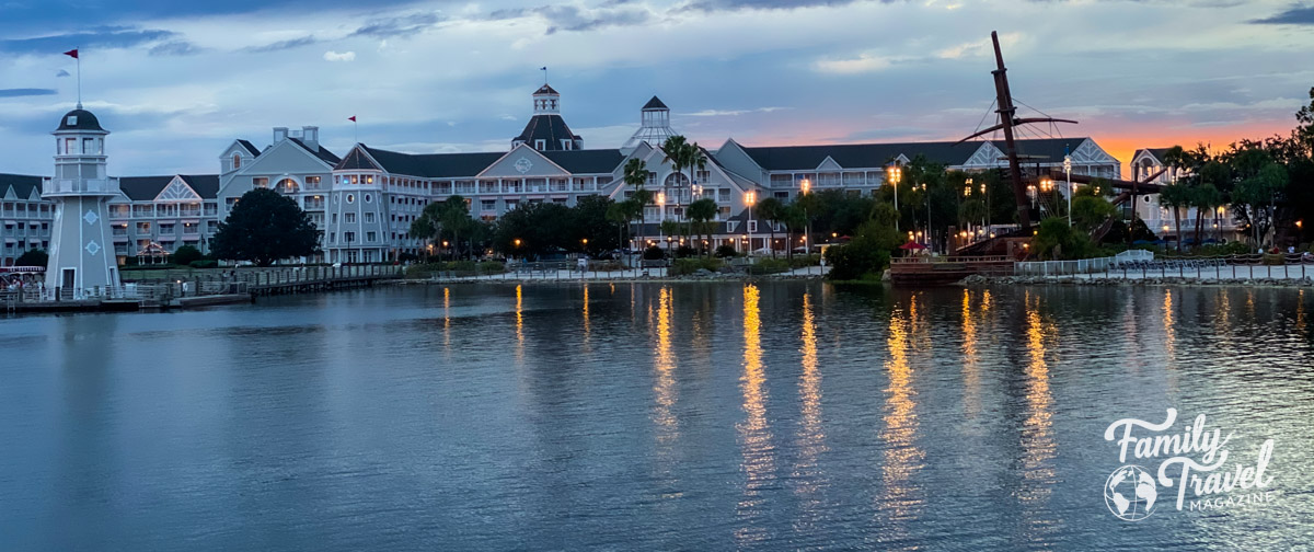 The Disney World Yacht Club from afar at sunset with lighthouse and buildings in front of the water