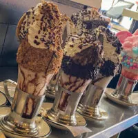 Four crazy shakes on a counter with chocolate, graham crackers, rock candy, and cotton candy