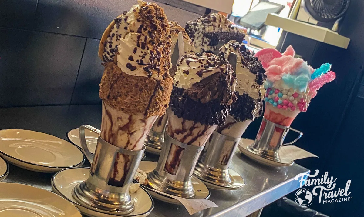 Four crazy shakes on a counter with chocolate, graham crackers, rock candy, and cotton candy