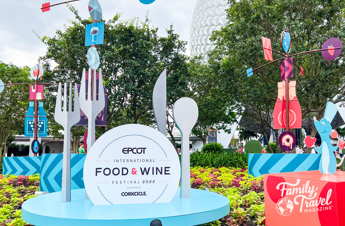 Large display advertising EPCOT International Food and Wine festival with large utensils, plates, glasses, food, and wine. 