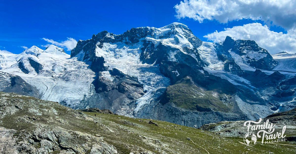 The snow covered Alps with blue sky and rocky mountain with green