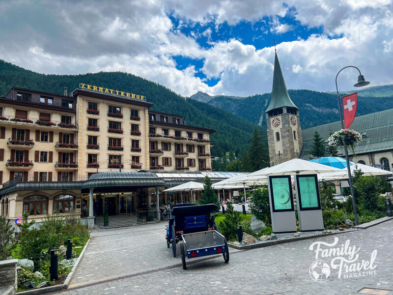 Exterior of Zermatterhof hotel with mountains in background and horse drawn carriage in the foreground