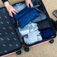 Hand packing a suitcase with clothes and toiletry bag.