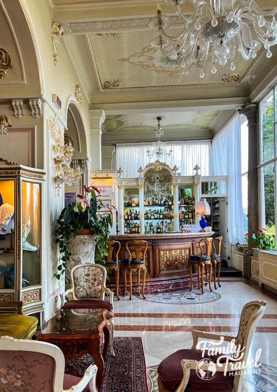 Ornate white bar with wooden bar chairs and tables in foreground. 