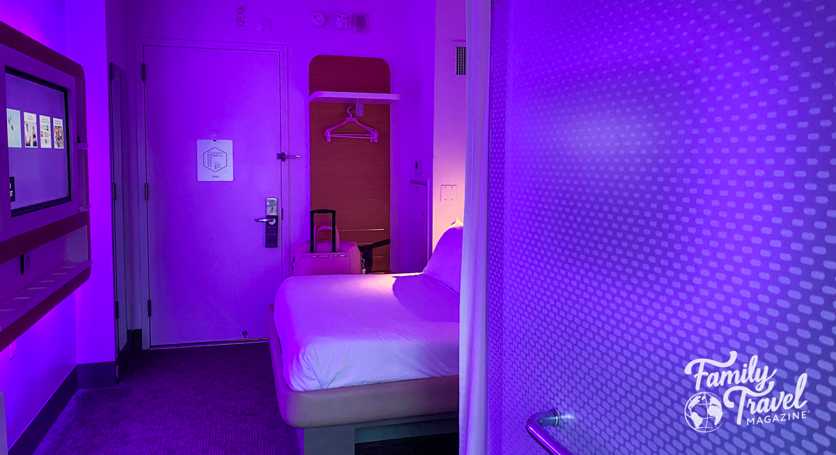 Hotel room at the Yotel with purple hint, showing tv, bed, small closet. 
