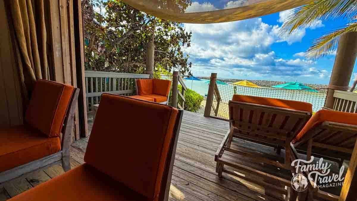 Beach cabana with orange cushioned chairs overlooking ocean and colorful umbrellas.