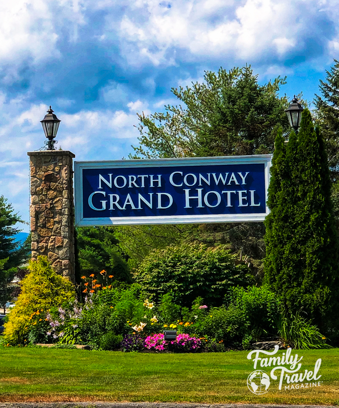 Sign at the entrance of the driveway for North Conway Grand Hotel with flowers and greenery. 
