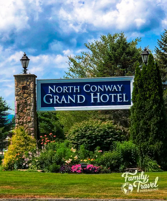Sign at the entrance of the driveway for North Conway Grand Hotel with flowers and greenery.