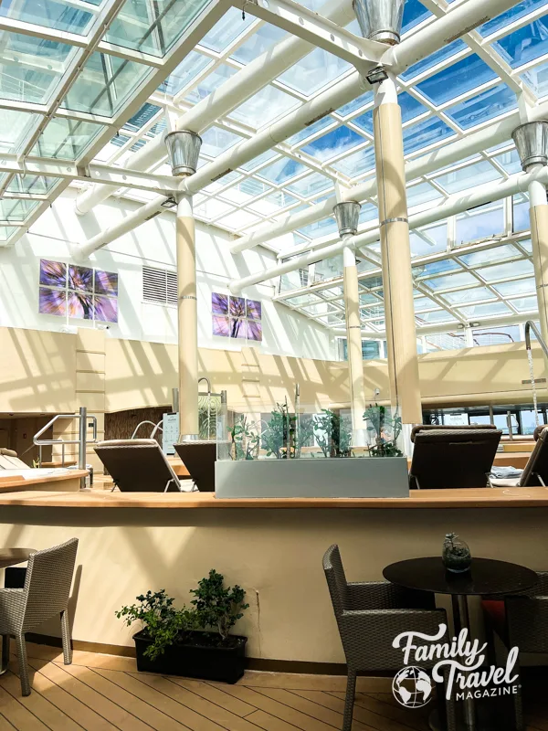 Solarium with a glass roof, lounge chairs, tables, and chairs around the pool deck. 