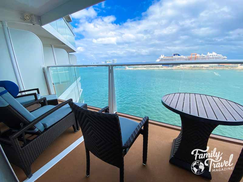 Cruise ship balcony with table and chairs overlooking port with ship in port