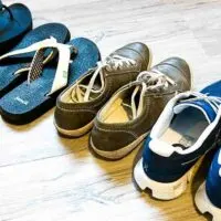 Four pairs of shoes in a row - two sandals, one leather sneakers, one traditional sneakers.